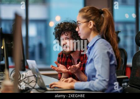 Geschäftskollegen, ein Mann und eine Frau, diskutieren Geschäftsstrategien, während sie aufmerksam auf einen Computermonitor schauen, Stockfoto