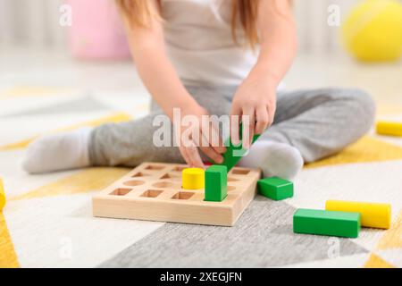 Kleines Mädchen, das mit geometrischen Holzfiguren auf dem Teppich spielt, Nahaufnahme. Kindergartenaktivitäten zur motorischen Entwicklung Stockfoto