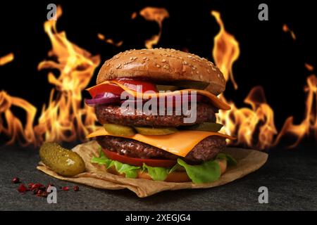 Leckerer Burger auf dunklem Tisch vor Flammen Stockfoto