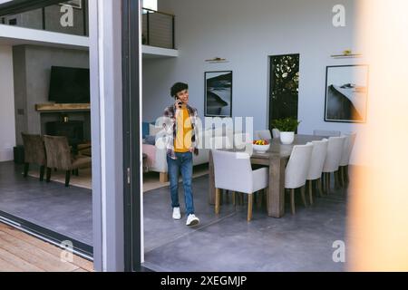 Mit dem Smartphone telefonieren, junger Mann, der zu Hause durch ein modernes Wohnzimmer geht Stockfoto