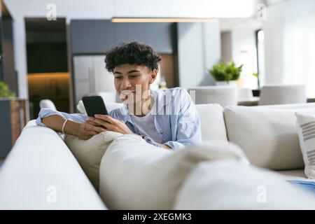 Mit dem Smartphone entspannt sich der Teenager auf der Couch in einem modernen Zuhause Stockfoto