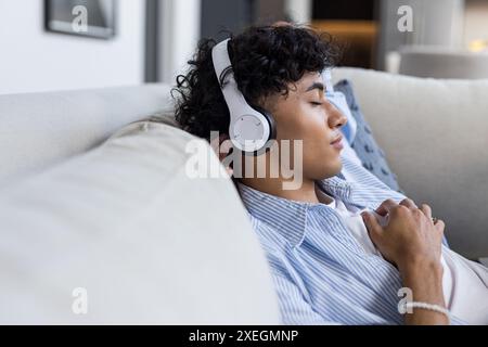 Entspannen auf der Couch, junger Mann hört Musik mit Kopfhörern, Augen geschlossen Stockfoto