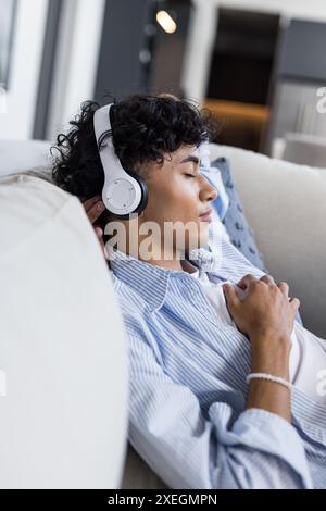 Entspannen auf der Couch, junger Mann hört Musik mit Kopfhörern, Augen geschlossen Stockfoto