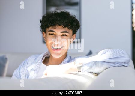 Lächelnder Teenager, der sich zu Hause auf dem Sofa entspannt und das Sonnenlicht genießt Stockfoto