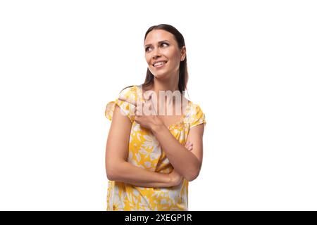 Eine junge Frau mit geradem schwarzem Haar in einem gelben Sommerkleid mit einem Druckmuster lächelt auf weißem Hintergrund Stockfoto