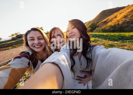 Eine Gruppe junger, attraktiver multiethnischer Frauen macht Selfies und lacht draußen. Lächelnde Mädchen verschiedener Rassen haben Spaß und Tak Stockfoto