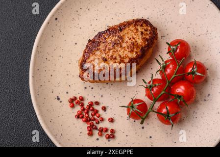 Köstliches frisch gebratenes vegetarisches Sojabohnenschnitzel mit Salz, Gewürzen und Kräutern mit Gemüse auf einer Keramikplatte auf dunklem Betonhintergrund Stockfoto