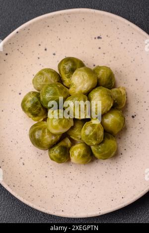 Köstliche gekochte Rosenkohl auf einer Keramikplatte auf dunklem Betonhintergrund Stockfoto