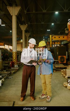 Vertikale Aufnahme eines männlichen Ingenieurs und einer Technikerin, die in der modernen Schwermaschinenindustrie zusammenarbeiten Stockfoto