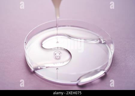 Serum oder Kosmetiköl fließt in eine transparente Schüssel auf violettem Hintergrund. Stockfoto