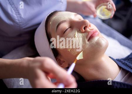 Der Schönheitsmeister wendet eine verjüngende Maske auf das Gesicht des Kunden an Stockfoto