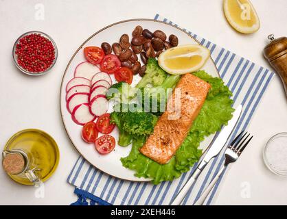 Gesundes Mittagessen mit gegrillter Forelle auf grünem Salat, neben Gemüse, Tomaten, Radieschen, Brokkoli und einer Portion Bohnen. Stockfoto