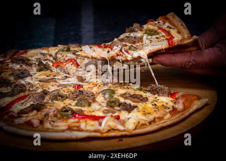 Nahaufnahme einer Hand, die ein Stück vegetarische Pizza mit Zwiebeln, Paprika und Gemüse auf einem Holzbrett nimmt. Schön Stockfoto