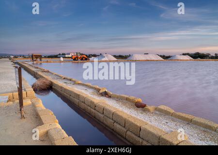 Ruhige Meersalzbecken und Wohnungen in der Nähe von Trapani und Paceco bei Sonnenuntergang mit Salzhaufen und Frontlader im Hintergrund Stockfoto