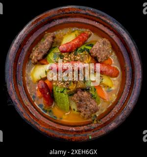 Blick von oben auf ein Tagine Royal Gericht mit Gemüse und verschiedenen Fleischsorten und orientalischen Gewürzen auf schwarzem Hintergrund Stockfoto