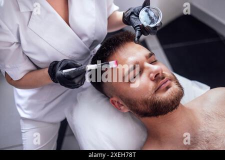 Schönheitsmeister wendet eine verjüngende Maske auf das Gesicht männlicher Klienten an. Hautstraffung Stockfoto