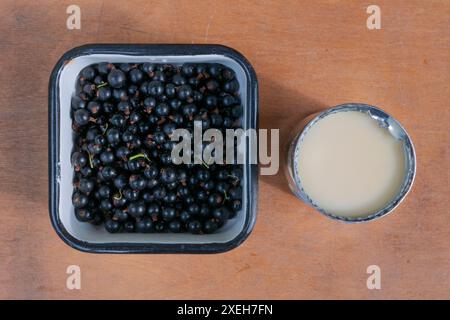 Geöffnete Dose Kondensmilch, schwarze Johannisbeere in Metallwaren auf braunem Holzhintergrund, Draufsicht. Das Konzept der gesunden Ernährung. Stockfoto