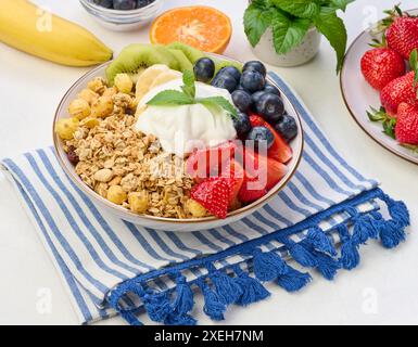 Müsli mit Erdbeeren, Kiwi, Banane und Heidelbeeren in einem runden Teller auf einem weißen Tisch. Stockfoto