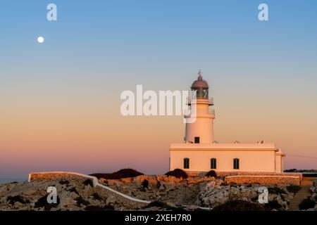 Senkrechte Ansicht des Leuchtturms Cap de Cavalleria auf Menorca bei Sonnenuntergang mit Vollmondaufgang Stockfoto