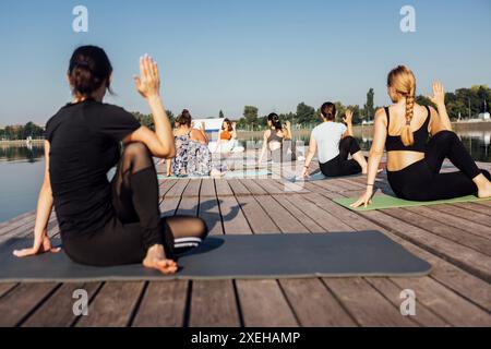 Yoga-Kurs am Morgen mit Lehrer am City Pier. Junge Frauen sitzen in der Pose eines Fischkönig und machen Ardha Matsyendrasana am Fluss Stockfoto