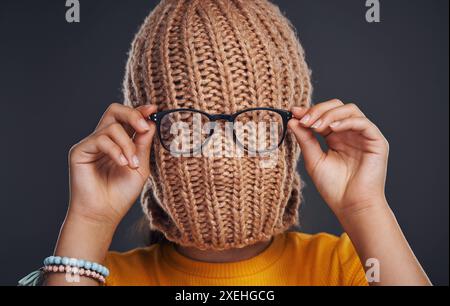 Mode, Cover und Mädchen mit Mütze im Studio mit Brille für lustige, Comic oder alberne Witze. Goofy, Style und Frauengesicht mit Strickmütze und Stockfoto