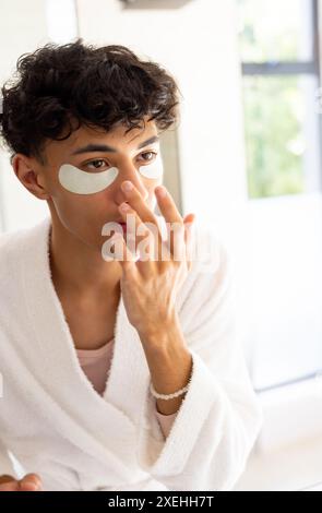 Hautpflege anwenden, junger Mann mit Augenflecken im Bad, Bademantel tragen Stockfoto