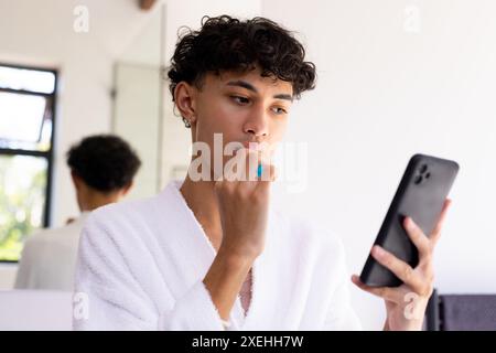 Zähne putzen, junger Mann im Bademantel mit Smartphone im Bad Stockfoto