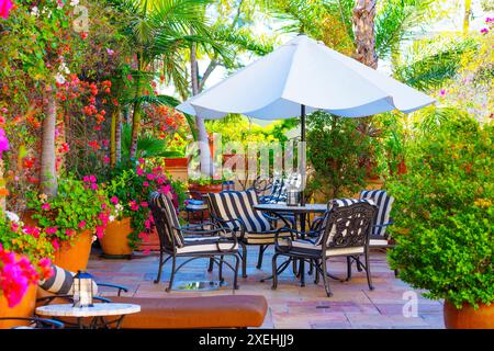 Ruhiger Essbereich im Freien mit Tisch und Stühlen unter einem weißen Sonnenschirm, umgeben von einem üppigen Garten. Stockfoto