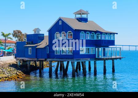 San Diego, Kalifornien - 16. April 2024: Blaues Holzhaus Seaport Village Café auf Stelzen über Wasser mit klarem Himmel Hintergrund. Stockfoto