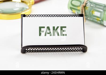 Fake News und digitales Kommunikationskonzept. GEFÄLSCHTE Schrift auf einer Visitenkarte in einer Komposition mit Euro-Banknoten und einer Lupe, die unscharf ist Stockfoto