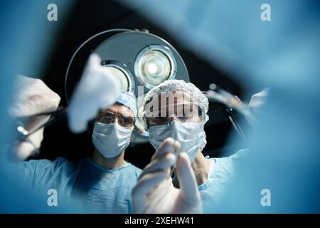 Tiefwinkelansicht zweier Chirurgen, die beim Tragen von Masken unter Operationslampen operieren und Werkzeuge halten Stockfoto