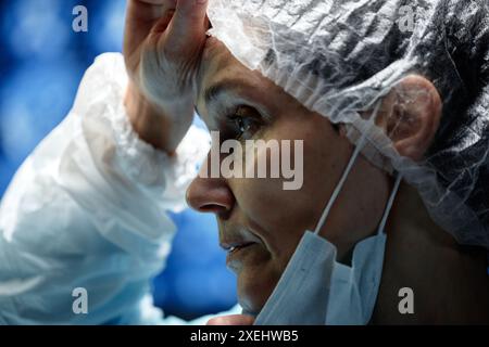 Dramatische Seitenaufnahmebildung eines erschöpften Chirurgen, der den Schweiß der Stirn während der Operation im Operationsraum reibt Stockfoto