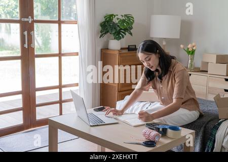 Beschäftigte asiatische Frau, die Paketzustellbox vorbereitet Versand zum Einkaufen online Notiz der Bestellung mit Laptop jungen Start-up sma Stockfoto