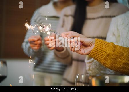 Fröhliche Freunde, die zu Hause Geburtstagsfeier genießen. Asiatische Freunde halten Lichter mit funkelndem Sparkler, die Weihnachten feiern Stockfoto