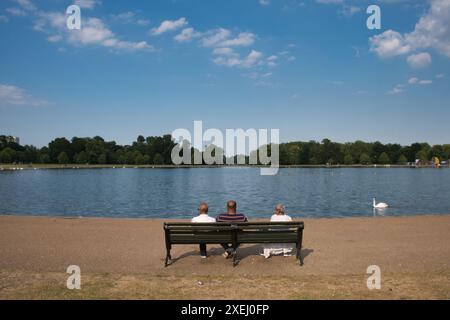 Touristen sitzen im Sommer auf einer Parkbank vor dem Round Pond in Kensington Palace, London Stockfoto