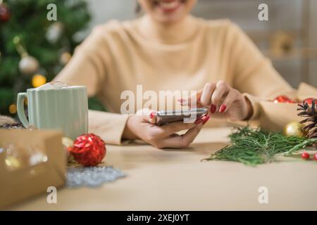 Glückliche junge Frau, die smartphoneÂ mobil sucht, verbringt Zeit vor dem Weihnachtsbaum zu Hause, um Neujahr und Chri zu feiern Stockfoto