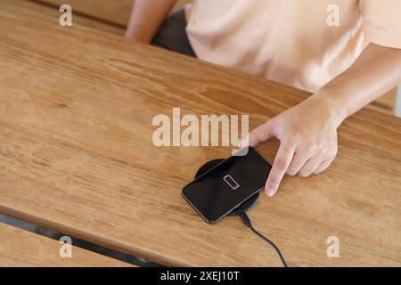 Laden des Mobiltelefonakkus mit drahtlosem Ladegerät im Tisch. Smartphone wird auf einem Ladepad aufgeladen. Mobiltelefon ne Stockfoto