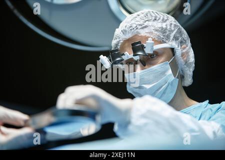 Tiefwinkelansicht bei reifer Chirurgin mit Maske und OP-Brille während der Operation Kopierraum Stockfoto