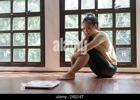 Traurige Frau mit Fettverstimmung gelangweilt von der Diät Gewichtsverlust failÂ Fettdiät und Waage traurige asiatische Frau auf Gewichtswaage zu Hause Gewicht c Stockfoto