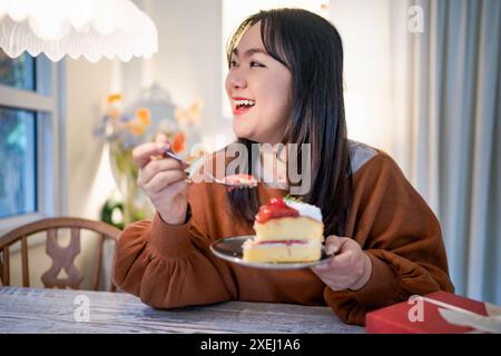 Schöne asiatische Frau, die leckeren Kuchen isst. Das Teenager-Mädchen isst den Kuchen. Stockfoto