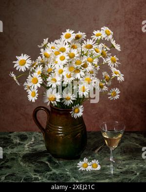 Ein großer Strauß weißer Gänseblümchen in einem braunen Tonkrug auf einem marmorgrünen Tisch. Neben dem Glas Weißwein und der Inschrift Liebe. Lustige Sommerpause Stockfoto