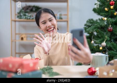 Glückliche junge Frau, die smartphoneÂ mobil sucht, verbringt Zeit vor dem Weihnachtsbaum zu Hause, um Neujahr und Chri zu feiern Stockfoto