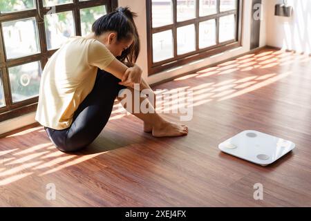 Traurige Frau mit Fettverstimmung gelangweilt von der Diät Gewichtsverlust failÂ Fettdiät und Waage traurige asiatische Frau auf Gewichtswaage zu Hause Gewicht c Stockfoto