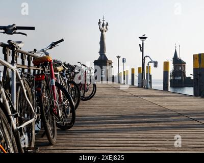 Eine Reihe von Fahrrädern, die entlang einer Holzpier geparkt werden, die Statue Imperia und ein historisches Gebäude im Hintergrund in Konstanz, Deutschland Stockfoto