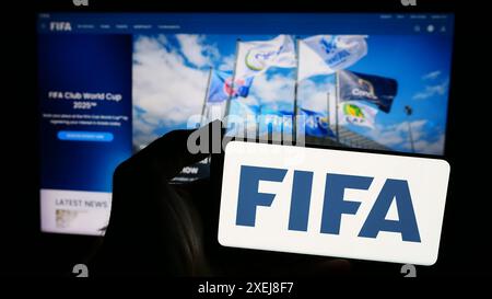 Person mit Smartphone und Logo der Federation Internationale de Football Association (FIFA) vor der Website. Schwerpunkt auf dem Display des Telefons. Stockfoto