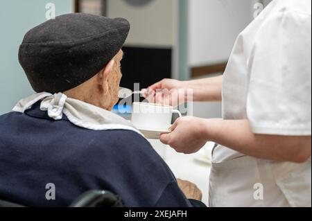 Seniorenmann, der im Pflegeheim von einer Pflegerin ernährt wird. Hochwertige Fotografie Stockfoto