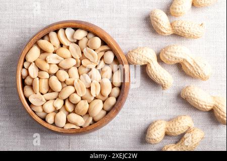 Geröstete und gesalzene Erdnüsse in einer Holzschale auf Leinenstoff. Verzehrfertige Snacks, hergestellt aus Früchten der Arachis hypogaea, auch bekannt als Erdnuss. Stockfoto