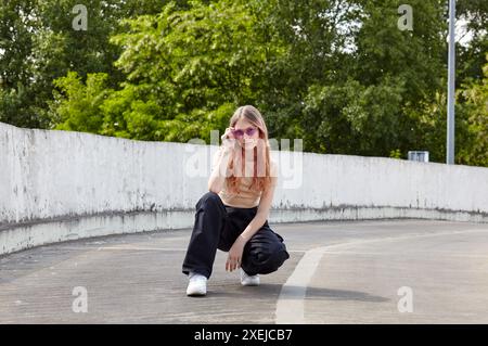 Porträt eines Teenager-Mädchens in Sonnenbrille, das auf der Straße sitzt. Hipster-Mädchen in trendigen Sommerkleidern. Glückliches Mädchen, das sich entspannt und sich amüsiert hat Stockfoto