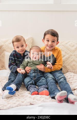 Lächelnde Brüder, die sich umarmen und lächeln, während sie auf dem Bett sitzen Stockfoto