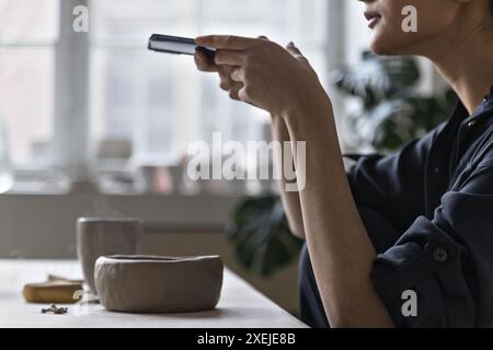 Asiatische Keramikerin fotografiert Tongeschirr per Telefon Stockfoto